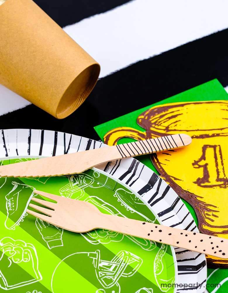 A closer look of a modern yet festive football party tablescape featuring football themed tableware from Momopartys including the football shaped paper placemat, the touchdown dessert plates, the trophy shaped napkins on a black striped table runner, making this a perfect inpo for a kid's football themed birthday party or a Superbowl party table decoration. 