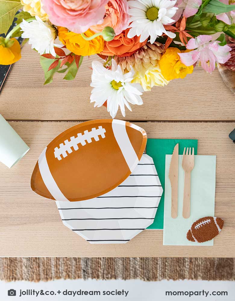A modern football party table filled with Momopartys's football themed party tableware by Daydream Society including the die-cut football shaped plate, black striped plate with green and mint napkins and party cups. In the center of the table there's a beautiful flower bouquet, all makes great inspirations for football themed celebrations, whether it's a kid's football birthday bash, a Super Bowl watching party or a Sunday football viewing party. 