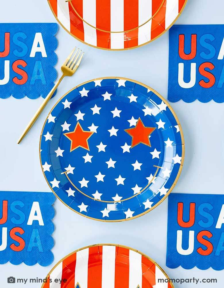A light blue table features Momopartys's Star & Stripe Smiley Paper Plates by My Mind's Eye. These plates come in a set of 8 in 2 designs, one with red stripes the other with blue stars. With a big smiley face and star eyes on them. Pair with 5" USA small blue napkins, they are perfect for a retro fun 4th of July party this summer!