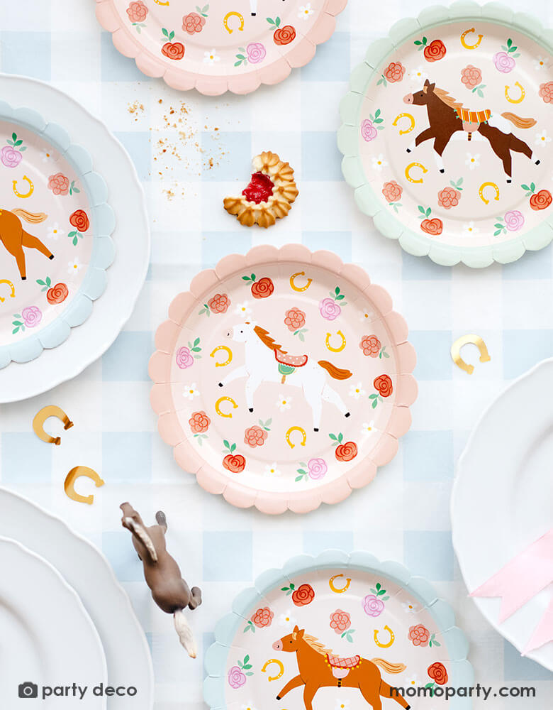 A overhead shot of a party table featuring Momopartys's 7" floral pony paper plates in 3 different colors and designs by Party Deco. The plates are placed on a light blue gingham tablecloth and around the paper plates are some gold horseshoe shaped confetti and some cookies, making this a perfect inspo for girl's pony or horse themed birthday party table decoration idea!