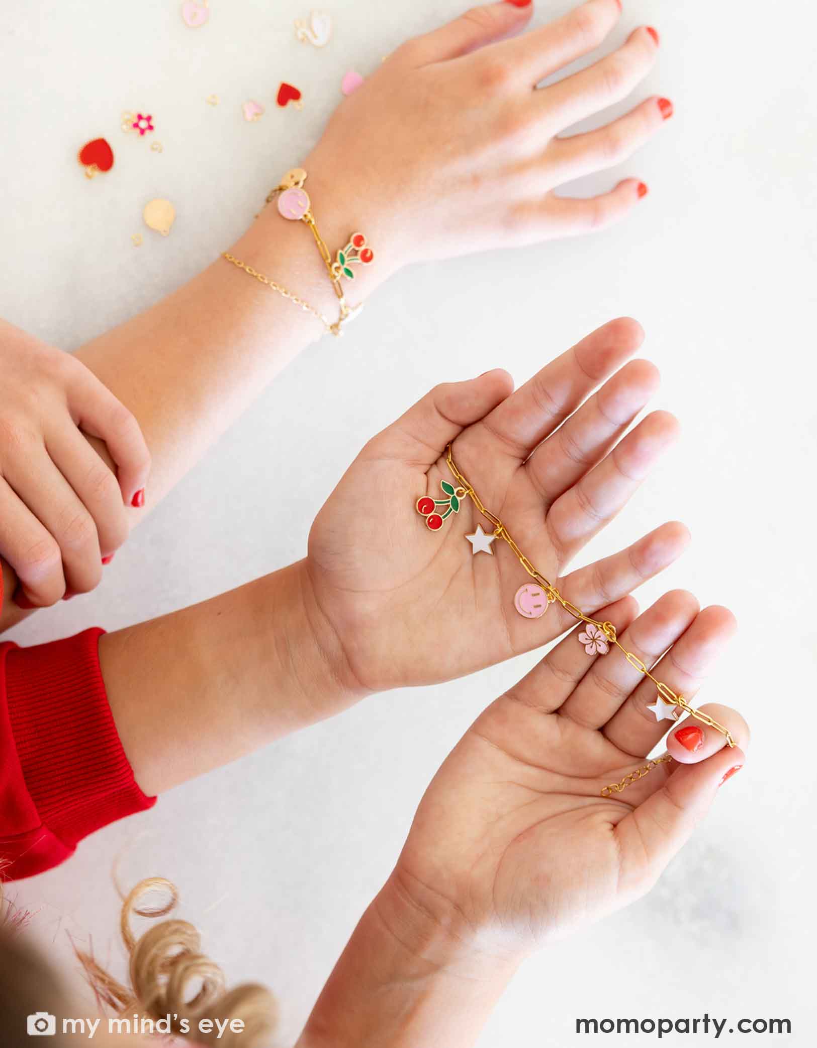 Children's hands wearing their gold bracelets with various charms from Momopartys against on a light background at a Valentine's Day themed sleep over party celebration.