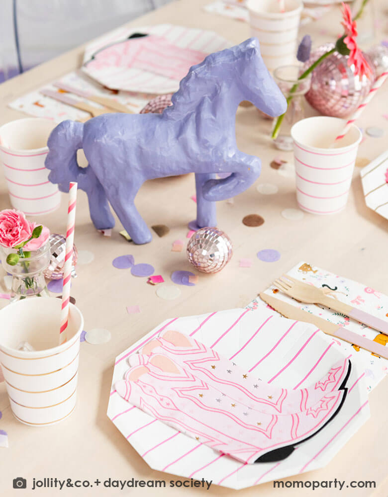 A girly cowgirl rodeo Western themed party table feature Momopartys's cowgirl boots shaped napkins, pink striped party plates, cups and cowgirl motif large napkins by Daydream Society. In the middle of the party table, there's a purple pony figure as the centerpiece which is surrounded by pink disco ball decorations, purple, pink and gold round confetti spread out the table, making this an adorable inspiration for girl's First Rodeo first birthday celebration or a cowgirl theme party for pony-loving girls!