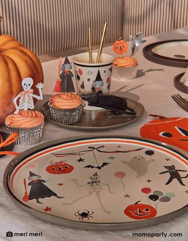 A vintage inspired Halloween table setting featuring Momopartys's This is Halloween! dinner plates, pumpkin shaped napkins, party cups, cupcakes topped with This is Halloween cupcake toppers. On the table there's a honeycomb mouse decoration making this a eerie yet playful tablescape. 