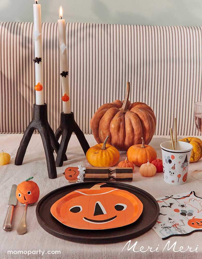  A modern Halloween party table featuring Momopartys's halloween themed tableware including the This is Halloween! pumpkin shaped plate, large napkins, a party cup a pumpkin surprise ball. Along with some real pumpkins in multiple colors and sizes and Halloween themed candles, this makes a great inspo for a modern kid's friendly Halloween table setting.
