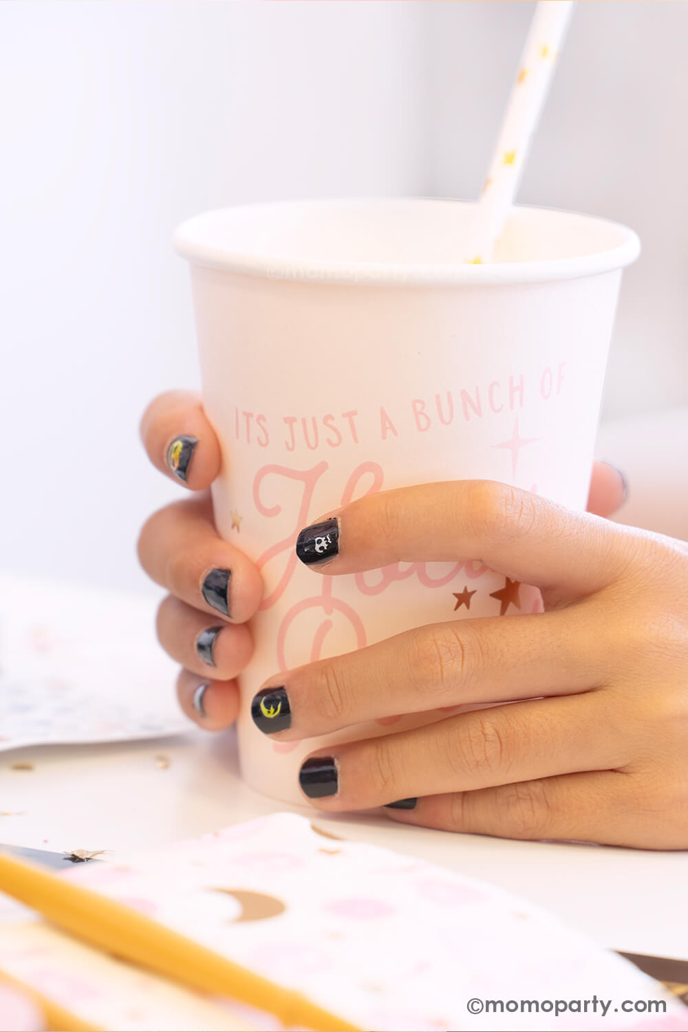 A kid's hand holding Momopartys's Hocus Pocus pink party cup in a witch themed Halloween party. The girl is wearing black nail polish with Halloween themed nail stickers including a crescent moon, a skull, a jack=o-lantern from the Snails Nail Polish Halloween Spooky Pack - which makes a perfect party favor or activity for kid's Halloween party.