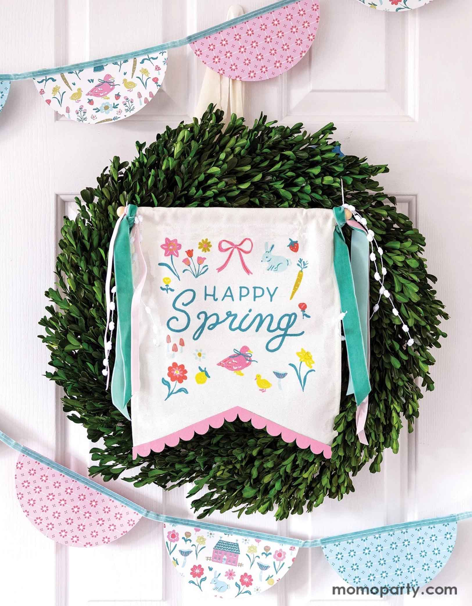 A white house door decorated with a wreath and Momopartys's 10.5" x 15" Happy Spring Canvas Banner by My Mind's Eye, featuring a playful "happy" message. With spring inspired illustrations like birds, flowers, bunnies, carrots and bows in pastel colors. Around the wreath there's a spring inspired bunting garland banner in pastel color and spring illustration motif, a prefect way to welcome a fresh and happy season of spring.