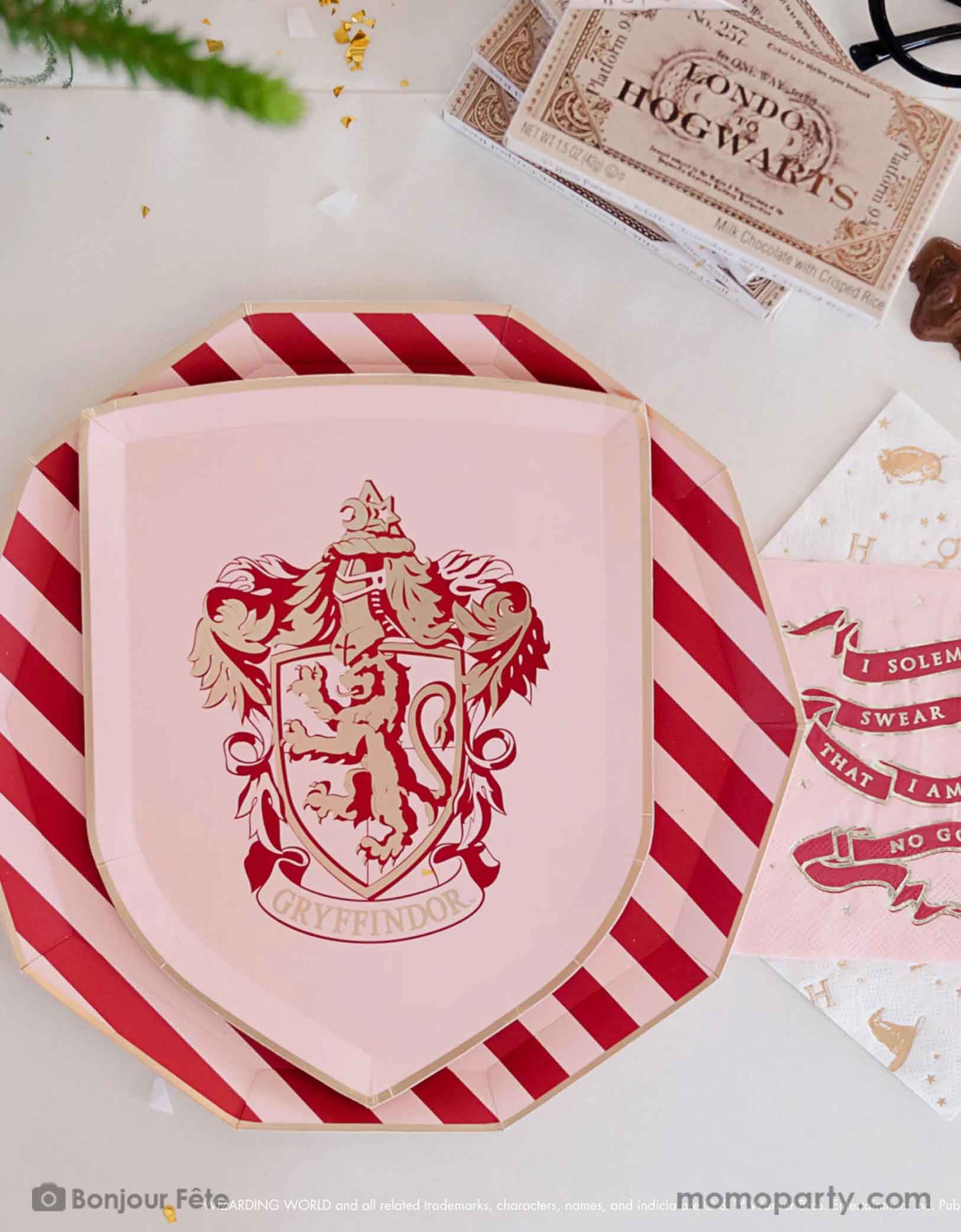 A beautiful and modern Harry Potter themed party tablescape features Momopartys's Harry Potter house pride shield-shaped 7" side plate with Gryffindor logo and color paired with 10.25 green striped dinner plate. Next to the plates are Harry Potter motif large napkins in gold foil and Slytherin green small napkins. On the table are some tickets Hogwarts and pretty flower arrangement - making this a great inspo for a modern Harry Potter themed birthday party celebration.