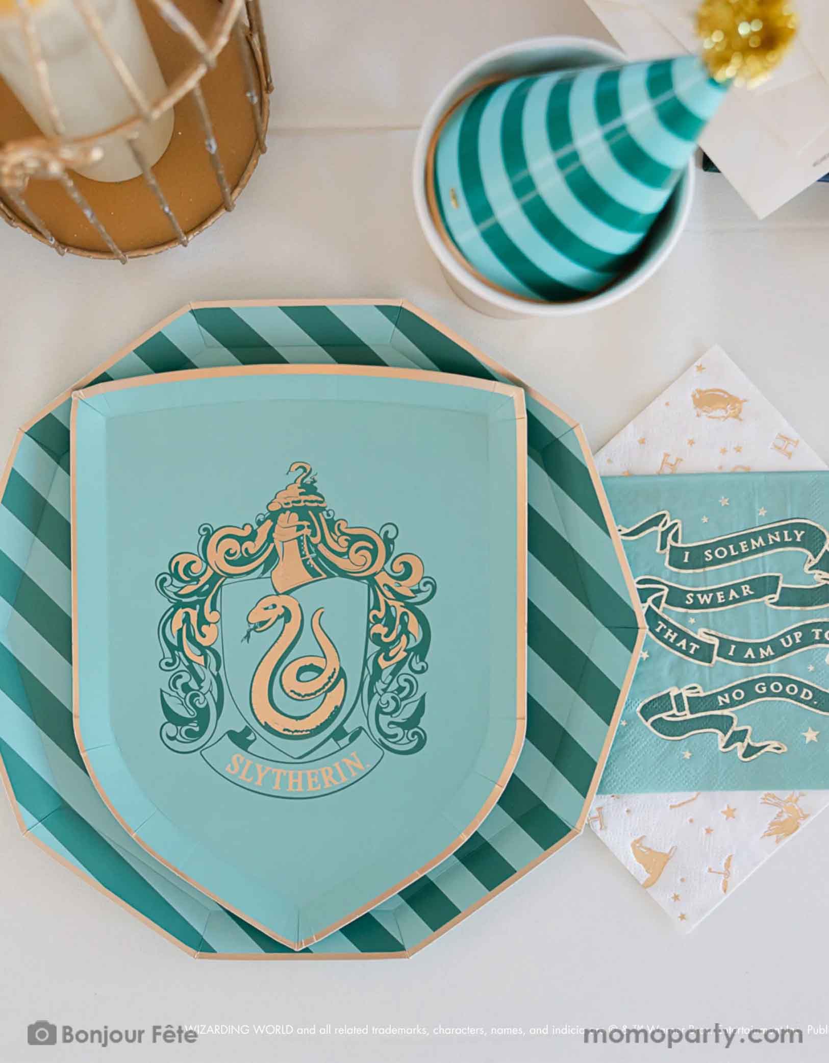 A beautiful and modern Harry Potter themed party tablescape features Momopartys's Harry Potter house pride shield-shaped 7" side plate with Slytherin logo and color paired with 10.25 green striped dinner plate. Next to the plates are Harry Potter motif large napkins in gold foil and Slytherin green small napkins. On the table there are some letters from Hogwarts, a bird cage for an owl and a green striped party hat  - making this a great inspo for a modern Harry Potter themed birthday party celebration.