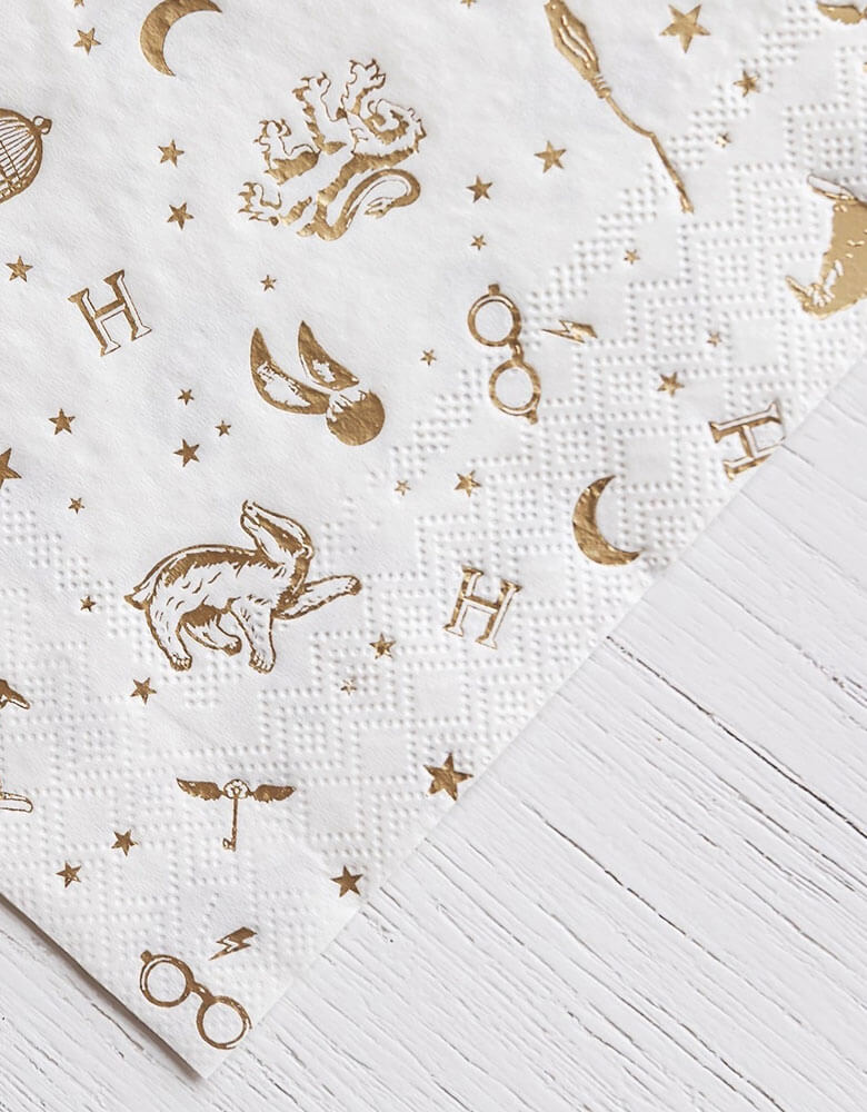 A close up shot of Momopartys's 6.5" x 6.5" Harry Potter Large Napkins by Bonjour Fete. Comes in a set of 24 napkins with elements including glasses, wizard hats, moons, stars and owls from Harry Potter in gold accent. Throw a magical bash with these Harry Potter party napkins. With whimsical gold accents, this modern design is perfect for any wizarding event.