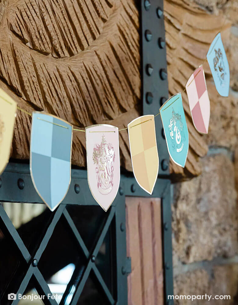 A close up shot of Momopartys's Harry Potter school pride multicolor party banner featuring different Harry Potter house symbols and colors including Hufflepuff, Slytherin, Gryffindor and Ravenclaw hung on outdoor on a brick wall at a Harry Potter themed party.