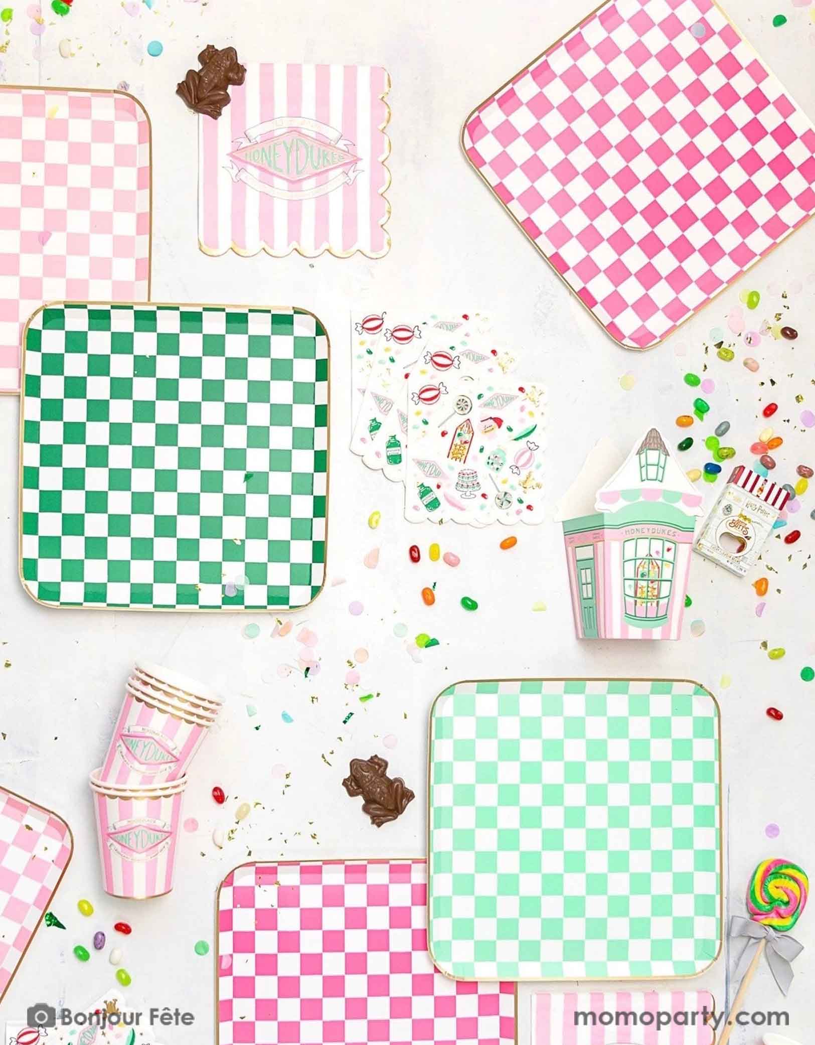 A Harry Potter themed tablescape featuring Momopartys's Harry Potter party collection including pink and green checkered dinner plates, pink striped Honeyduke large napkins, party cups and treat boxes. With chocolate frogs, Bertie Bott's Every Flavour Beans, lollipops and colorful confetti, this makes a festive scene for kid's Harry Potter themed birthday celebration.