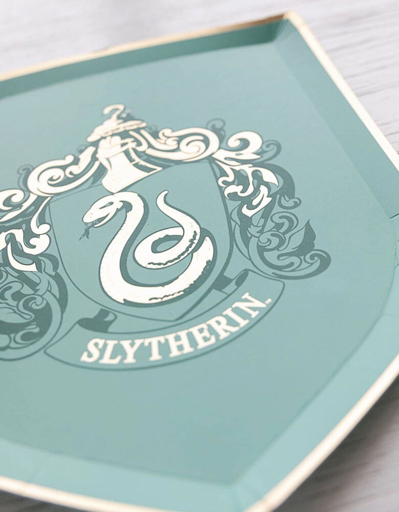 A close up shot of Momopartys's 7" Harry Potter House Pride Small Plates by Bonjour Fete. Comes in a set of 8 shield-shaped paper plates in 4 colors/designs each represent the color and symbol of the houses including Hufflepuff, Gryffindor, Slytherin and Ravenclaw. These plates are prefect for your Harry Potter themed celebration, be it a birthday party, a Halloween bash or a magic themed gathering.