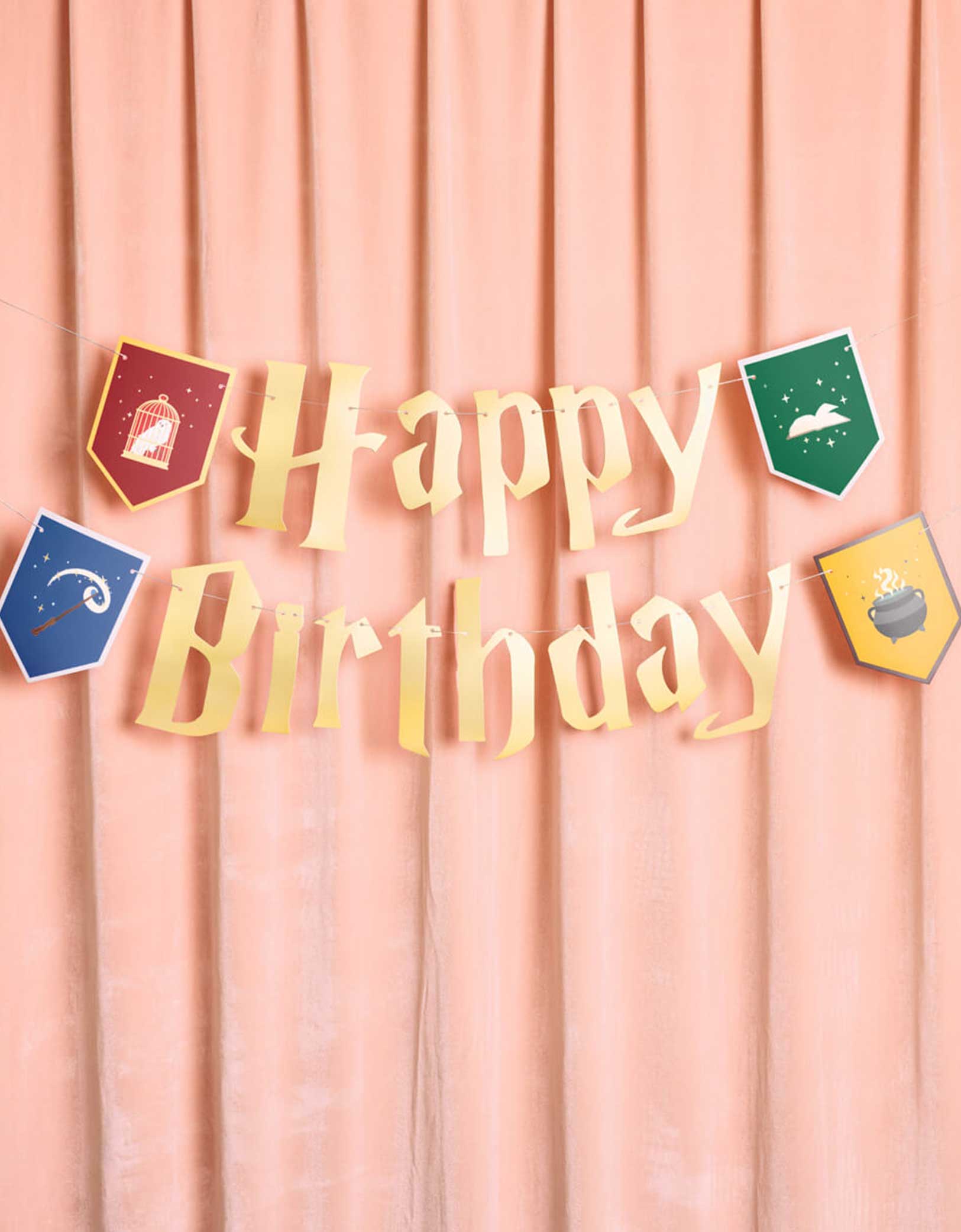 Momo Party's 5' Harry Potter themed Wizard Birthday Party Banner by Xo, Fetti. Inspired by the Hogwarts in Harry Potter, this party banner features "Happy Birthday" letters with red, green, blue and  yellow Harry Potter colored house crest shaped pendants with designs of an owl, a wand, a spell book, and a cauldron.  It's perfect for kid's Harry Potter themed birthday party!