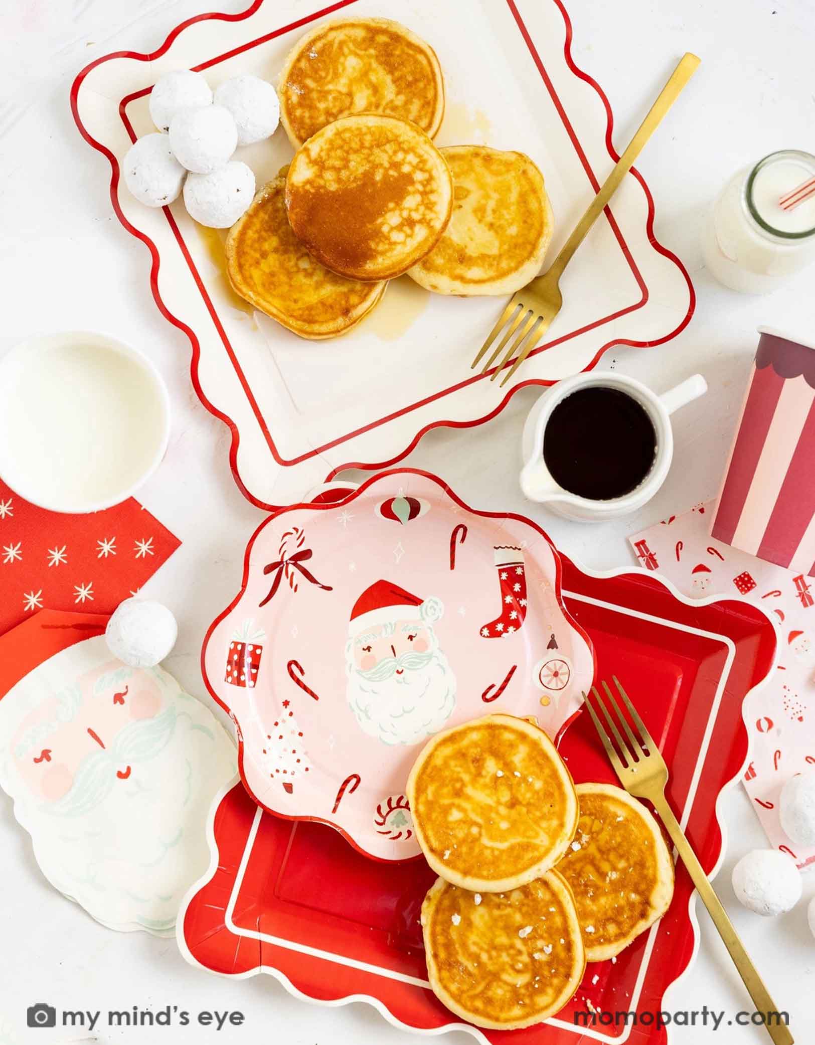 A festive Christmas breakfast scene with pancakes, milk, coffee, and Momopartys's Dear Santa party collection including the scallop square plates in red and cream, scallop round table with Santa and candy cane designs, Santa shaped napkins and red striped party cups on a white table.
