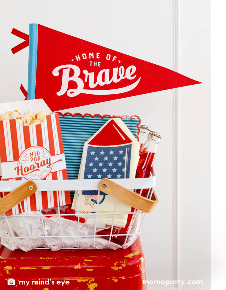 An occasion bin filled with festive patriotic themed party goods including Momopartys's 15" Home of the Brave red felt pennant by My Mind's Eye, blue stripe scallop-edged plates, rocket shaped guest napkins, red striped popcorn treat boxes with "hip hip hooray" on it, these are perfect decorations for a Memorial Day celebration or 4th of July Independence Day party!