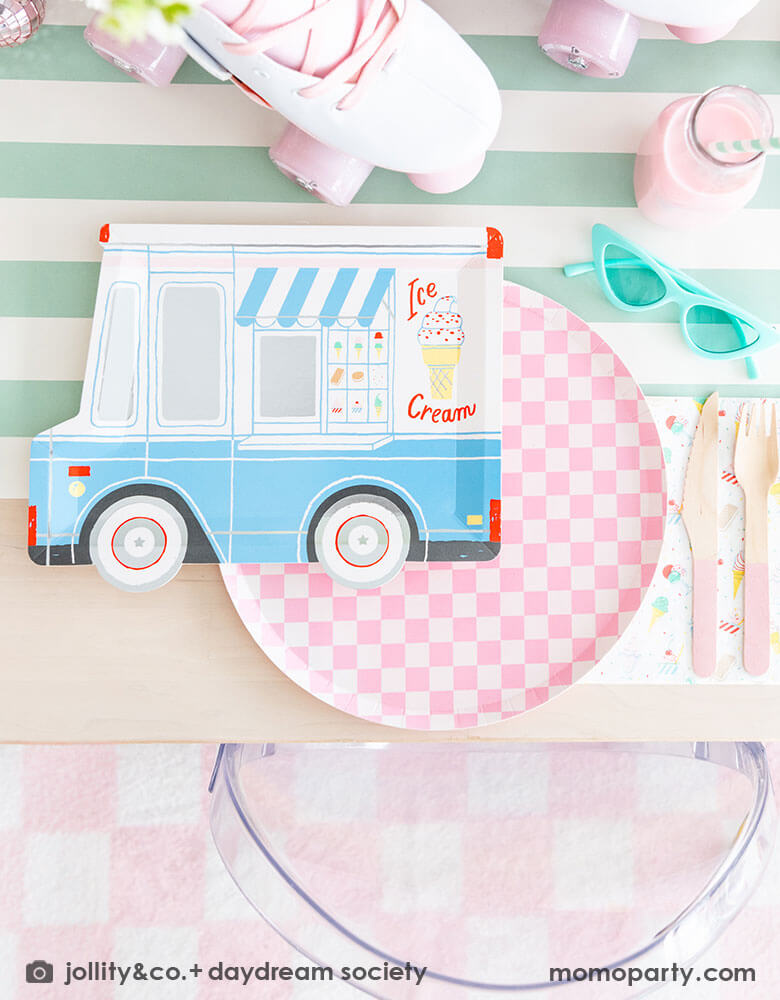 An adorable kid's ice cream themed birthday party tablescape featuring Momopartys's ice cream truck shaped plate, the pink checkered plate, the ice cream icon napkin and pink wooden cutlery on a mint striped table runner. Around the placeset there are some summer inspired decoration like a pair of mint sunglasses, a pair of pink roller skates, some milk bottles with gum ball pink drinks, making this a cute, fun and festive ice cream social for friends and family!