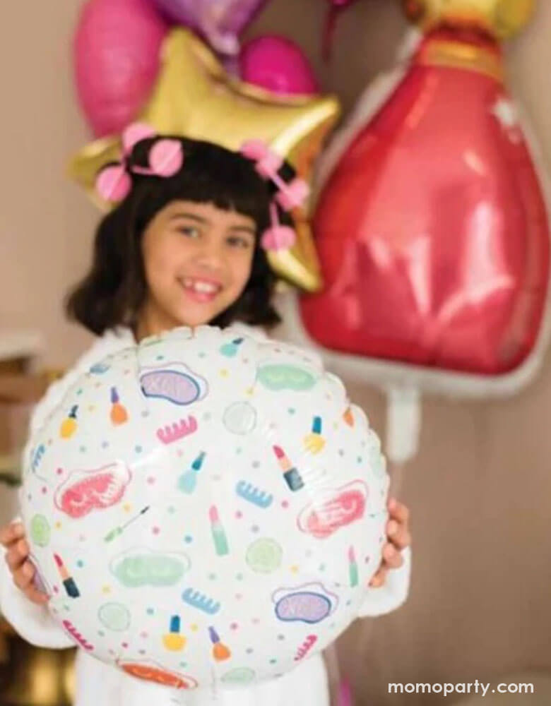 A school aged girl in her robe and hair curls holding Momopartys's 18" spa party round foil balloon by Anagram Balloons. In the back there are some colorful birthday party balloons including a nail polish bottle shaped foil balloon, some star shaped balloons in gold, pink and purple - a fun party decoration for girl's sleepover or slumber parties!