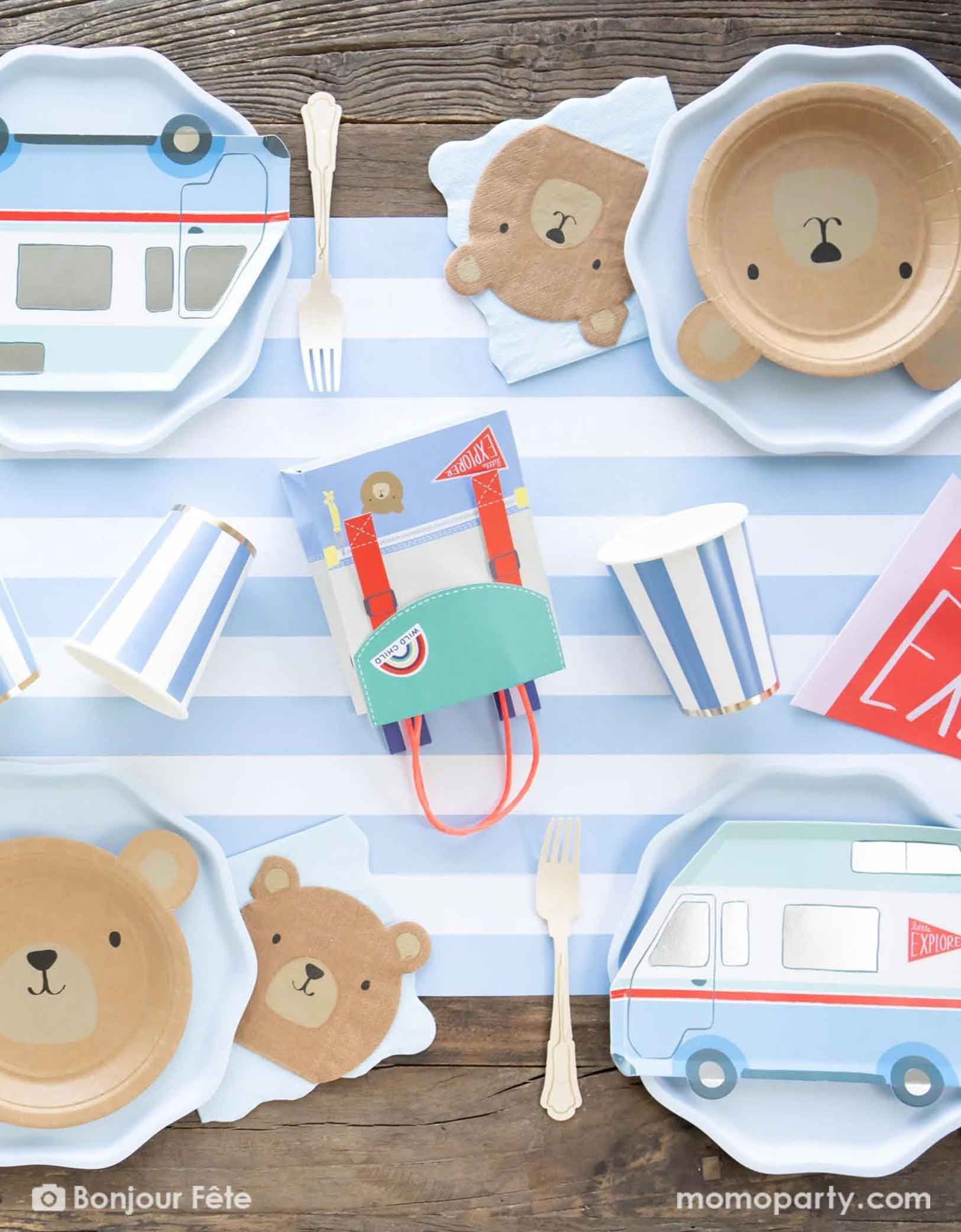 An adorable boy camping party table set featuring multiple camping themed tableware from Momopartys including the bear shaped plates and napkins, camping van shaped plates and a backpack shaped favor bag by Meri Meri from Momopartys. With blue striped party cups and matching paper table runner on top of a wooden picnic table, this gives a perfect inspiration idea for a cute kid's camping themed birthday celebration, be it a "One Happy Camper"  or a "Wild One" first birthday party. 