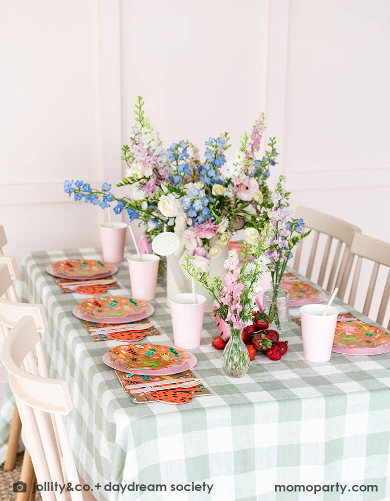 A cute kid's bug insect themed party table set up featuring Momopartys's backyard bug patterned plates, napkins paired with pink party cups and plates. With an olive green gingham tablecloth under and a beautiful flower bouquet, this makes a perfect inspiration for a modern take of a kid's bug themed celebration.