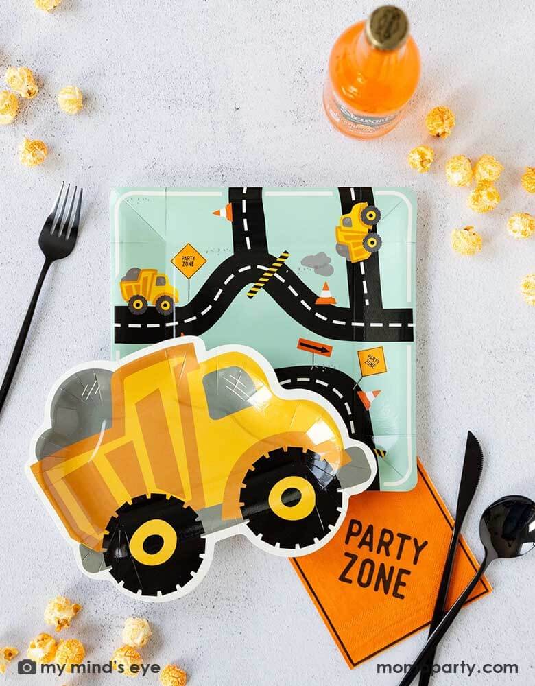 A kid's construction themed party tablescape featuring Momopartys's construction themed party supplies including the square truck road plate, the truck shaped plate, a party zone napkin, black cutlery, orange soda bottle and some popcorn around. Making this a perfect inspo for a kid's festive construction themed birthday party.