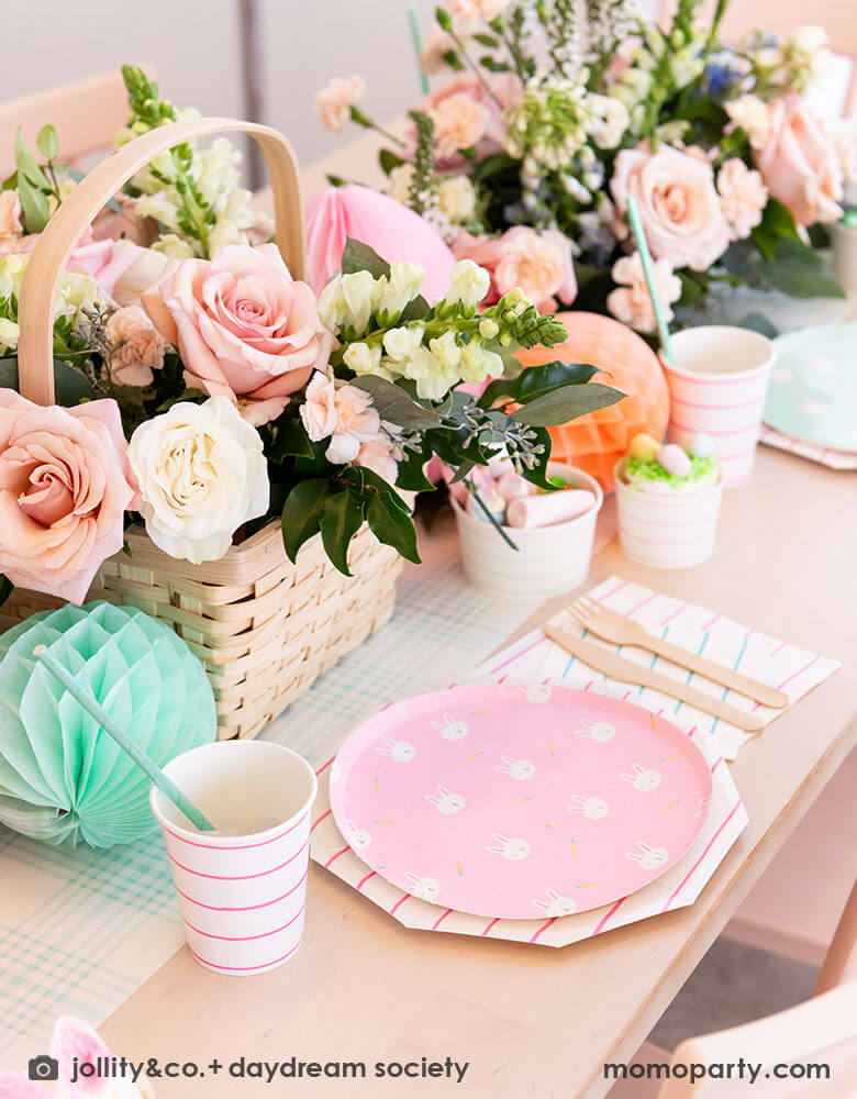 A beautiful Easter brunch table features Momopartys's Easter fun small plates along with striped party plates, cups, and napkins. In the middle of the table lays a blue gingham table runner which has baskets of spring flower arrangement and egg shaped honeycomb decorations in pastel colors, making this an adorable inspo for a Easter party tablesetting.