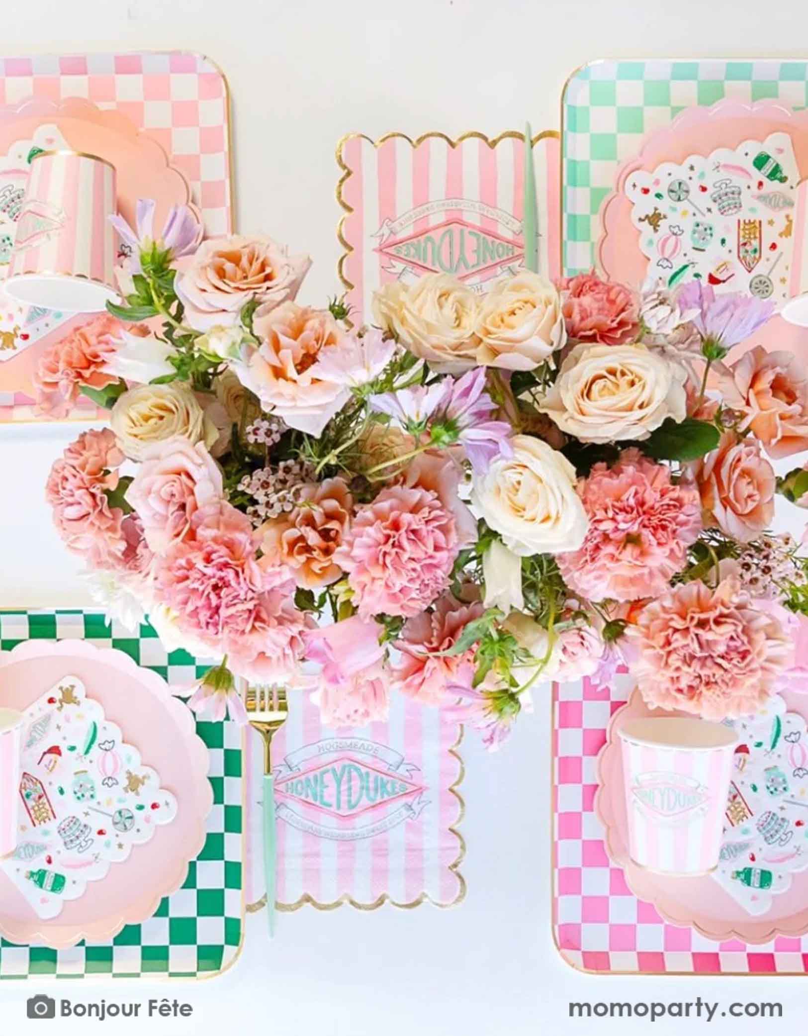A modern and beautiful table setting featuring Harry Potter Honeydukes themed party supplies in pink and green  including pink and green checkered dinner plates, pink striped Honeyduke large napkins, party cups and matching napkins. With a beautiful floral bouquet in the middle, this makes a modern and elegant party table setting for kid's girly Harry Potter themed birthday celebration.