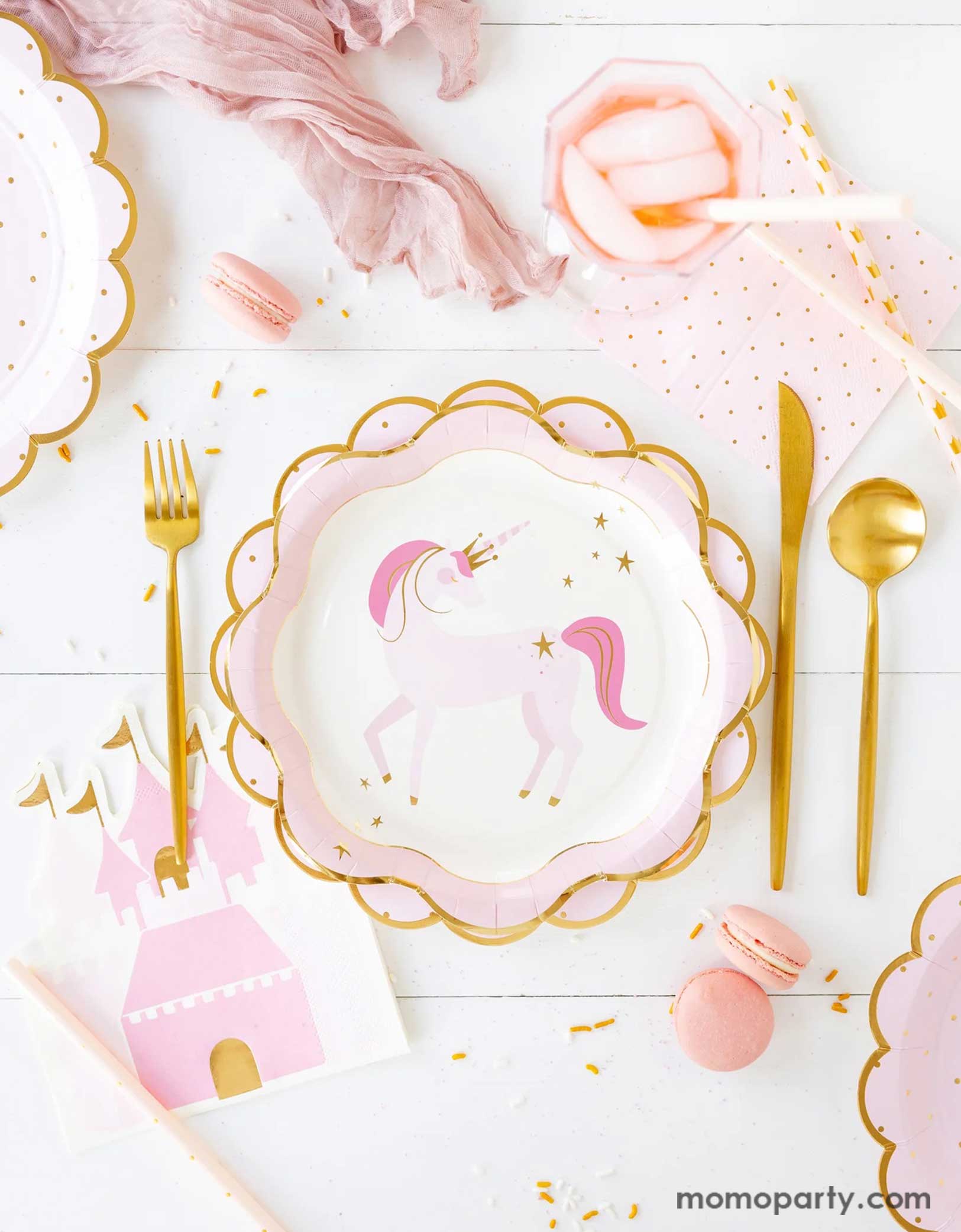 A princess and unicorn themed party tablescape featuring Momopartys's pink party tableware including unicorn plates, princess castle shaped guest napkins, pink polka dot napkins and matching scalloped edged paper plates. Along with pink macarons and gold foil cutlery set, this table is ready for your little royal and her guests in a playful birthday bash!