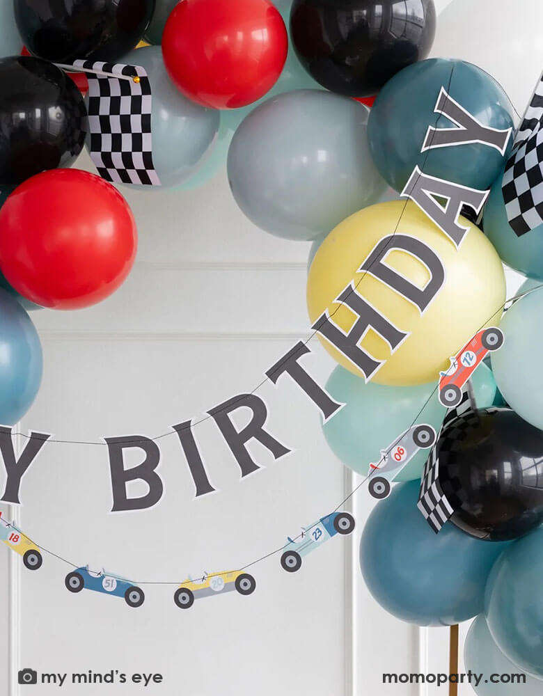 A kid's race car themed birthday party decoration set up features Momopartys's 4ft & 6ft Miles Per Hour race car happy birthday banner set, a balloon garland in dark blue, light blue, gray, red and black colors adorned with checkered race car flags, making this a perfect inspo for modern kid's car themed parties, be it a "Fast One" first birthday party, a "Two Fast" second birthday party, "speed limit 3" or "grand 3" third birthday or a "Need Four Speed" fourth birthday bash.