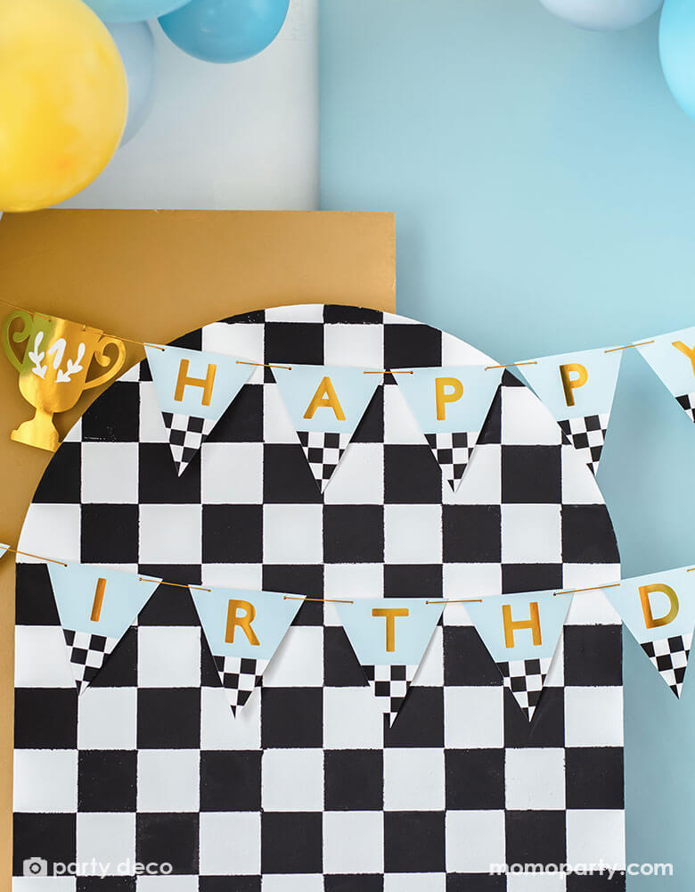 A close up of a race car checkered party backdrop adorned with Momopartys's trophy race car happy birthday banner - This banner celebrates the big day with "Happy Birthday" written on it with trophy pennants.