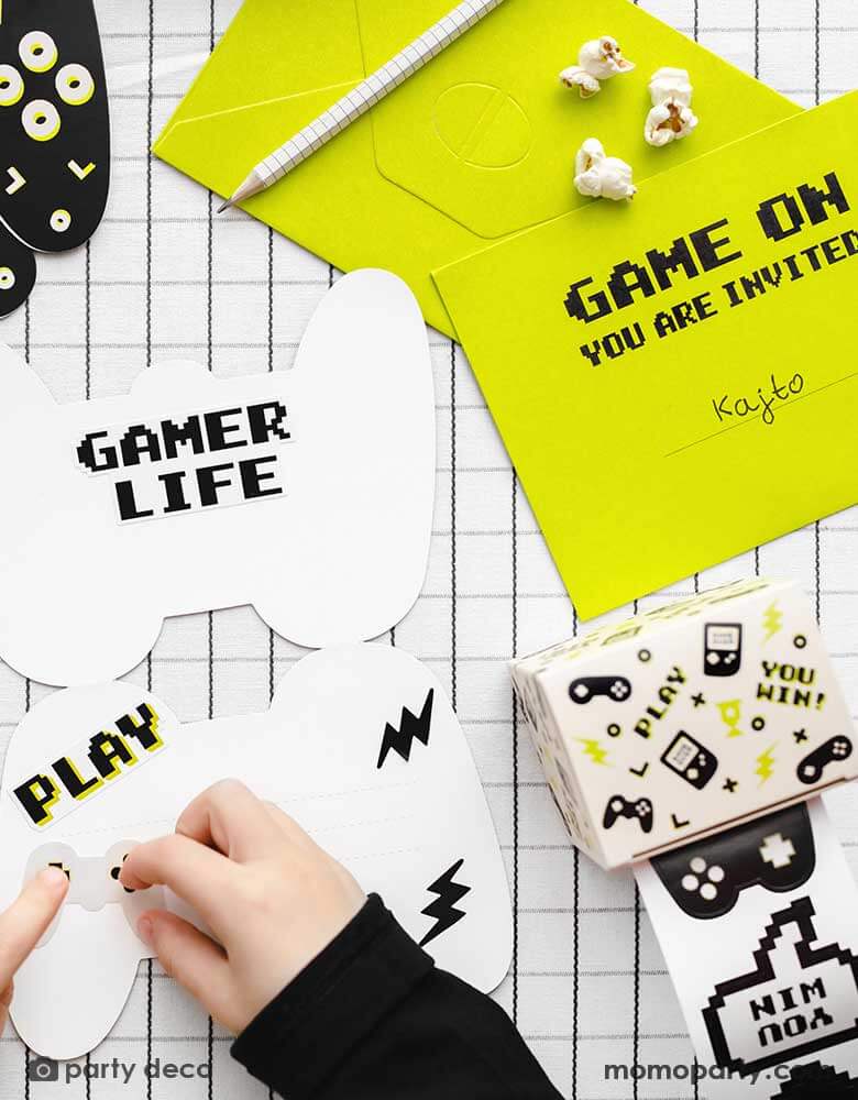 A boy making a video game themed birthday invitation using Momopartys's Gamer Sticker Roll by Party Deco. Each roll includes 36 stickers in 18 design including video game devices and game controllers. These stickers are perfect for party favors and activities at any gaming party.