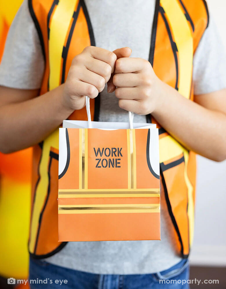 A boy dressed up as a construction worker holding Momopartys's 5.5" x 5" x 4" Construction Vest Treat Bags by My Mind's Eye. These treat bags will make any party a blast with their playful construction vest design. Perfect for construction themed parties or just for fun, this set will be a hit with kids and adults alike. 