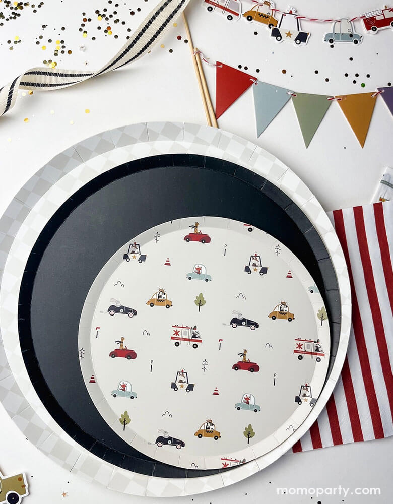 A festive kid's vehicle themed party tablescape featuring Momopartys's 10.25" light grey checkered dinner plate, 9" navy large plate and a round side paper plate with multiple colorful vehicle illustrations on it including ambulance trucks, police cars, taxi cars, and cars by Josi James. Around the party plates are red striped paper napkins, birthday cake pennant flag and vehicle cake toppers, along with ribbons and confetti, this makes a great inspiration for a preschool boy's birthday party decoration!
