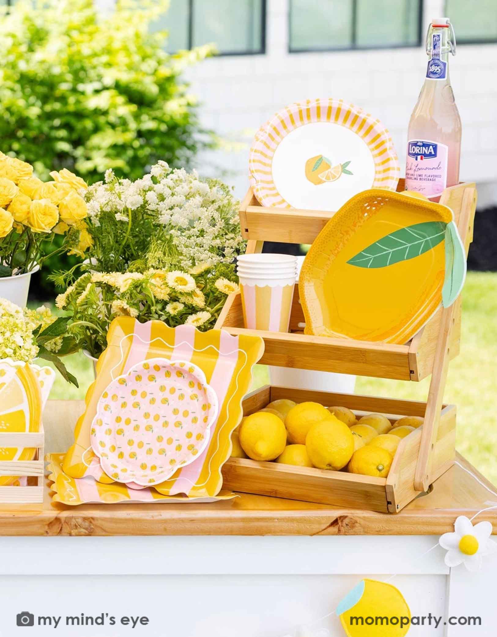 Decorative lemon garland with lemons and daisy flowers on a lemonade wooden cart with a bottle of lemonade, lemons, lemon themed party tablewares including lemon shaped plates, party cups, and napkins from Momopartys in a wooden crate. With some adorable yellow and white flowers, this makes a cute set up for a lemon themed celebration, be it a baby shower, a kid's birthday or a summer Amalfi Coast inspired bridal shower. 