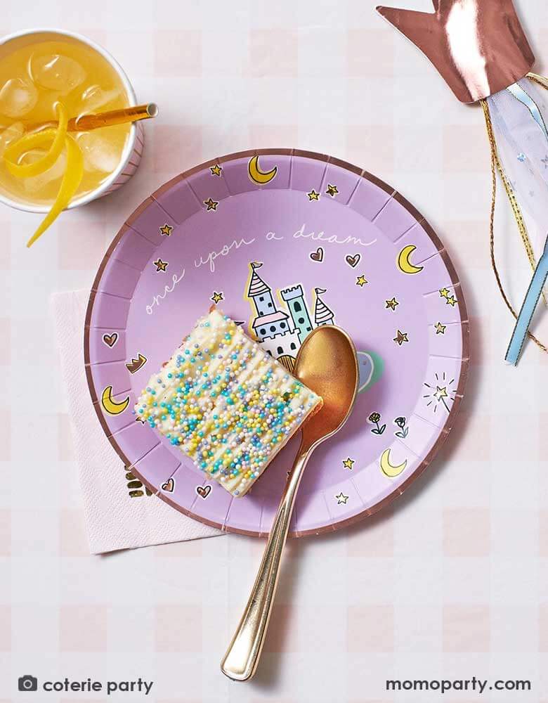 An adorable kid's princess table features Momopartys's 8.5' x 4.5' pink gingham tablecloth by Coterie. On the tablecloth there is a princess themed round paper plates with castles design on it and a slice of cake with colorful sprinkles on it. Next to the plate is a party cup filled with orange juice and a rose gold crown wand. Making this a perfect inspo for a little girl's princess themed birthday celebration.