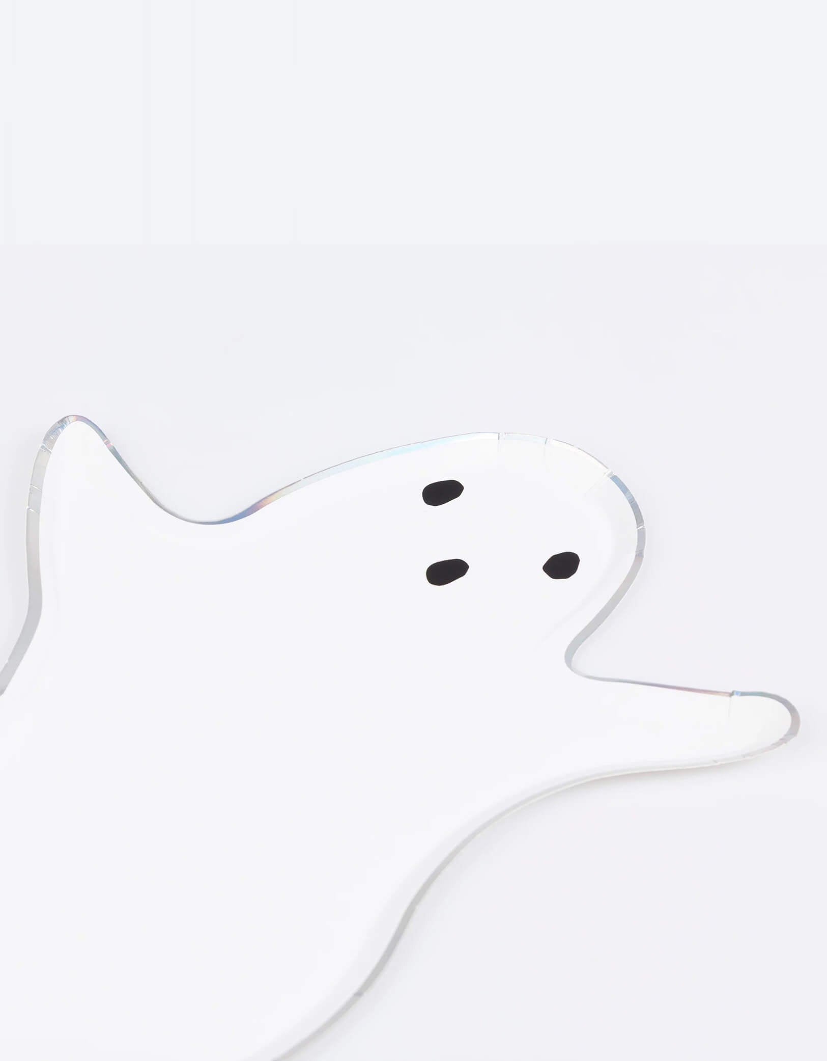A close up of Momopartys's 9" x 13.25" ghost shaped plate by Meri Meri on a white background.  Designed with a classic floaty ghost silhouette and a dazzling silver holographic foil border, they create a hauntingly cool effect. Perfect for kid-friendly gatherings or creepy cocktail parties!