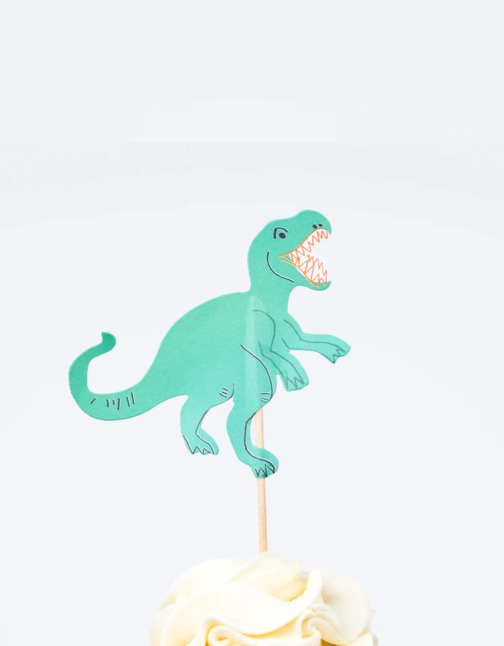 A cupcake decorated with Momopartys's T-rex cupcake topper by Meri Meri. This fun kit also makes a great gift for kids who love to bake.