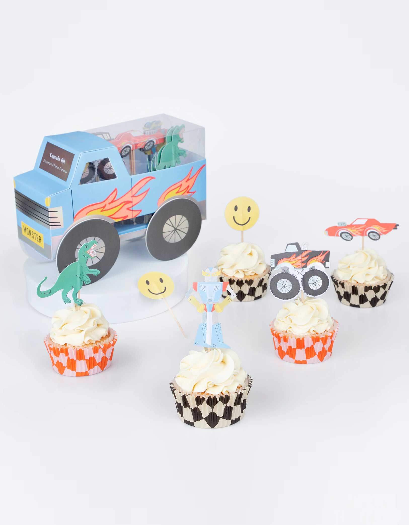 A few cupcakes decorated with Momopartys's Monster Truck Cupcake Kit by Meri Meri, featuring iconic retro toy cupcake toppers, including 5 designs of a monster truck, a car, a robot, a T-rex and a smiley face and checked cupcake cases, to make the most fun and tasty treats. Next to the cupcakes is the monster truck shaped kit box which makes a centerpiece to delight the birthday boy or girl and their guests. 