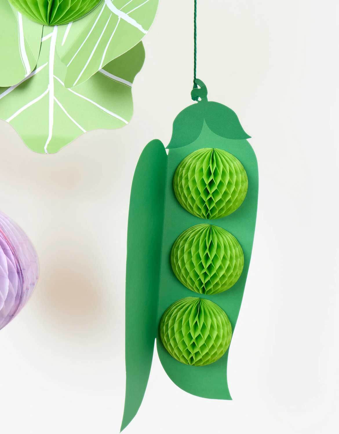 A close up of a green pea hanging honeycomb decoration from Momopartys's decorative paper hanging vegetable honeycomb decoration set by Meri Meri on a white background.