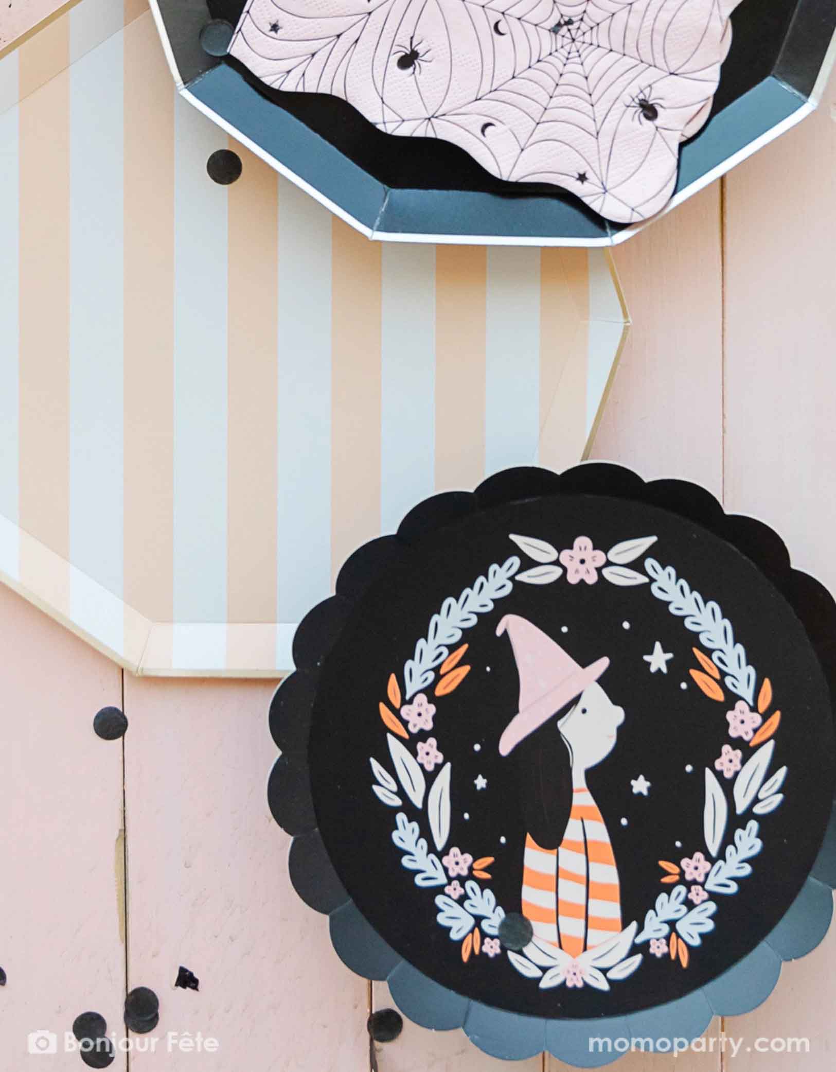 An overhead shot of a Halloween themed party table featuring Momopartys's sweet peach cabana striped decagon dinner plate, black decagon dinner plate and that witch small plate, with black confetti around to add some spooky yet chic vibe for a kid's friendly Halloween bash.