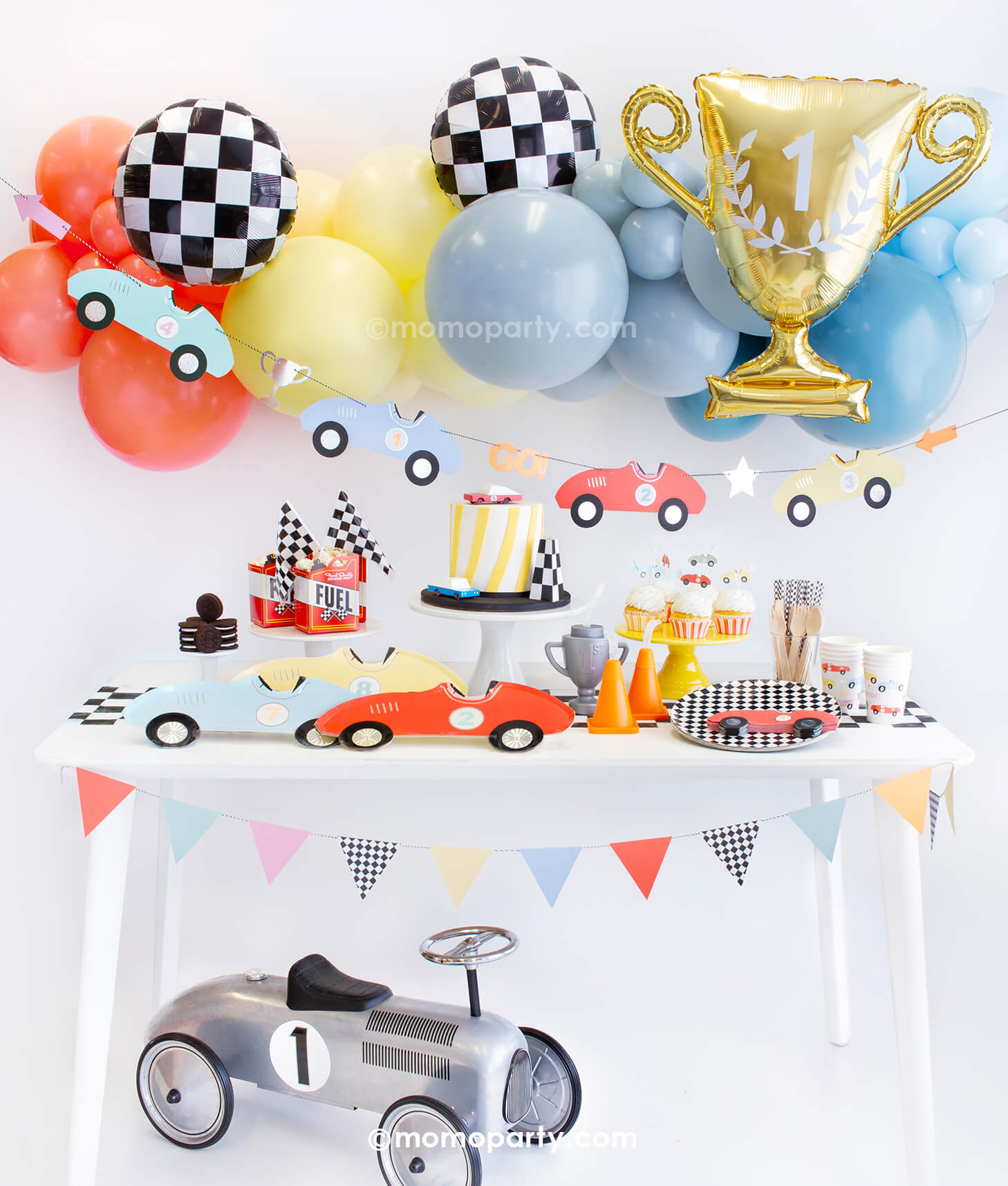 Momopartys Race Car Box featuring Meri Meri race car paper plates, race car shape napkins, race car graphic party paper cups, checkered round side plates, race car cupcake kit, candy car as cake topper, Fuel treat favor box with popcorns as tableware, colorful balloon cloud, race car party garland in pastel colors, checkerboard foil balloons and a trophy shaped foil balloon as decorations, all makes a great inspo for kid's modern race car party or a "Fast One" first birthday celebration.