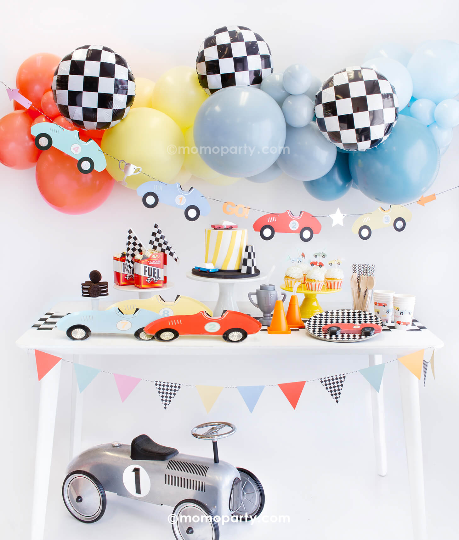 Momopartys Race Car Box, set up inspiration with Meri Meri race car paper plates, race car shape napkins, race car graphic party paper cups, checkered round side plates, neon confetti flag cupcake kit, candy car as cake topper, Fuel treat favor box with popcorns as tableware, colorful balloon cloud, race car party garland with party pennants in pastel colors, checkerboard foil balloon as decorations for modern Race car, car themed "Two Fast" second birthday party or a "Fast One" first birthday party.
