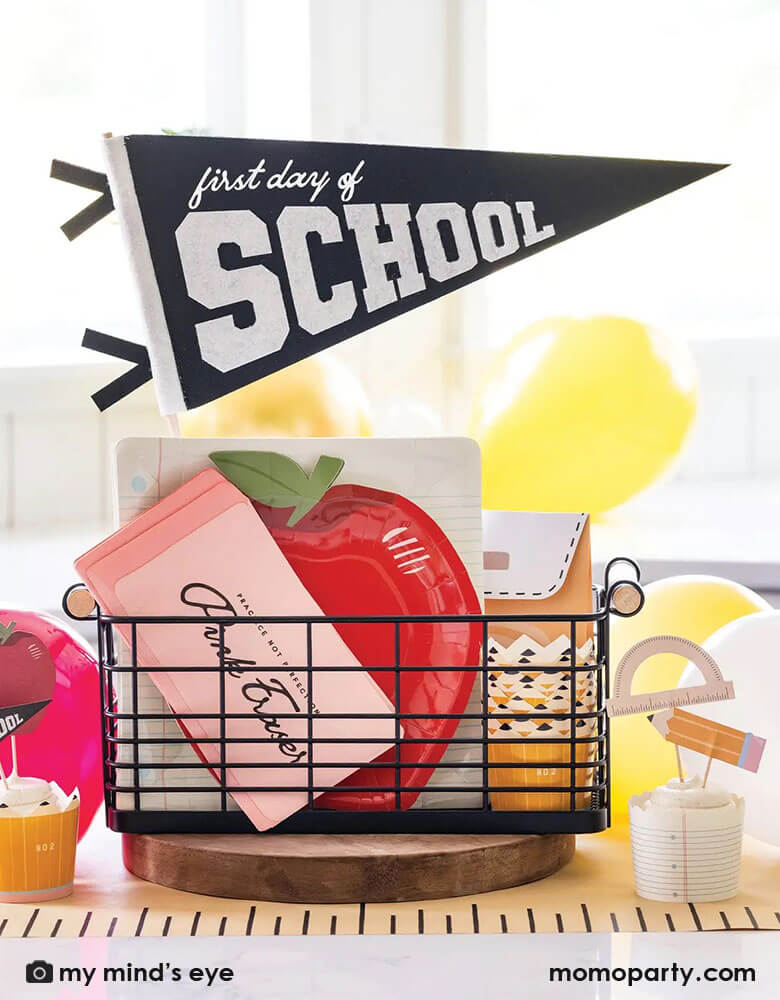 An occasional bin filled with kid's back to school party supplies including Momopartys's first day of school felt pennant, apple shaped plates, notebook plates, eraser napkins, back to school food cup kit and a ruler table runner by My Mind's Eye. All in all, it creates a great inspo and idea for kid's back to school celebration.