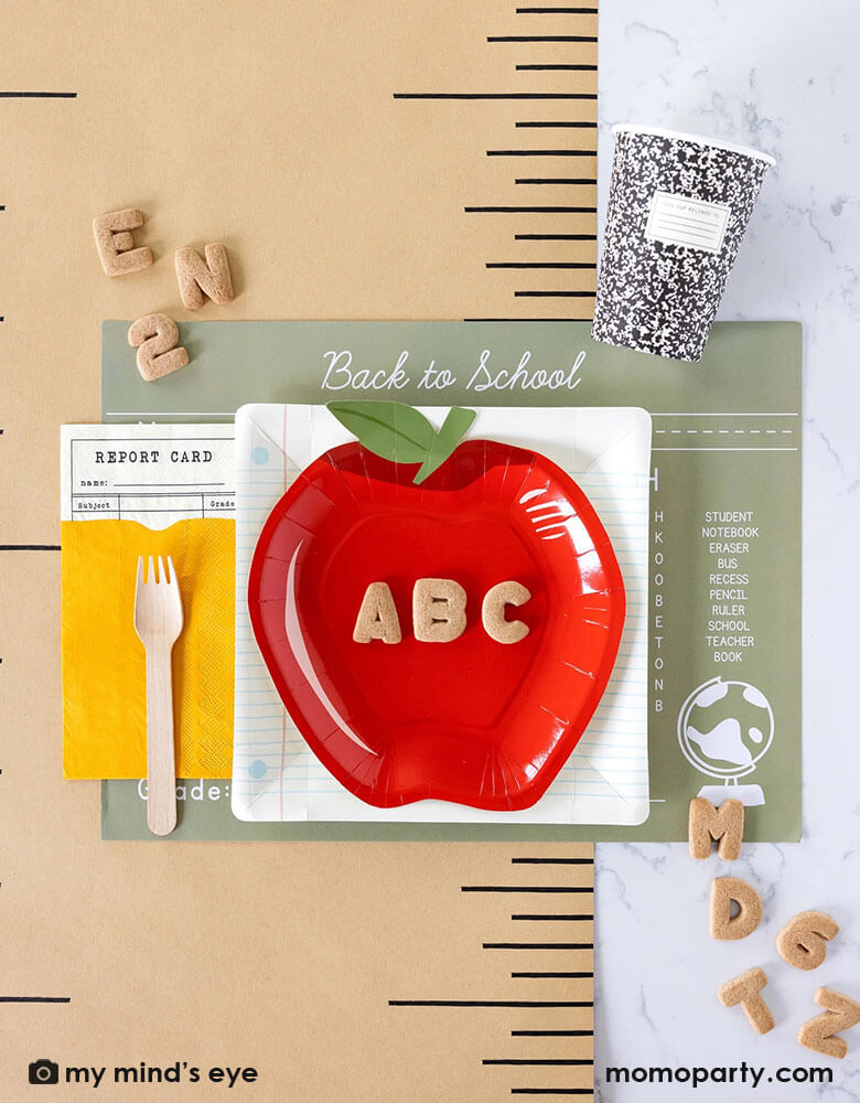 A clean and modern back to school party, first day of school celebration tablescape featuring Momopartys's back to school ruler runner, composition notebook party cups, back to school tablemats, back to school notebook square plates, apple shaped plates and report card shaped napkins, along with ABC alphabet cookies around them, it makes a great inspiration for kid's back to school celebration.