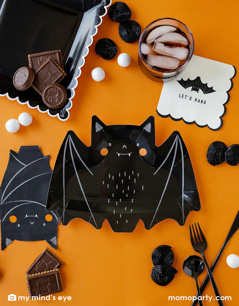A classic Halloween black and orange table featuring Momopartys's 10.5" x 8.5" bat shaped plates, napkins and black square plates with white scalloped edge. Along the tableware, there are some black and white Halloween treats including candies, chocolates and gum balls, makes it a great party inspiration for kid's friendly Halloween party ideas.