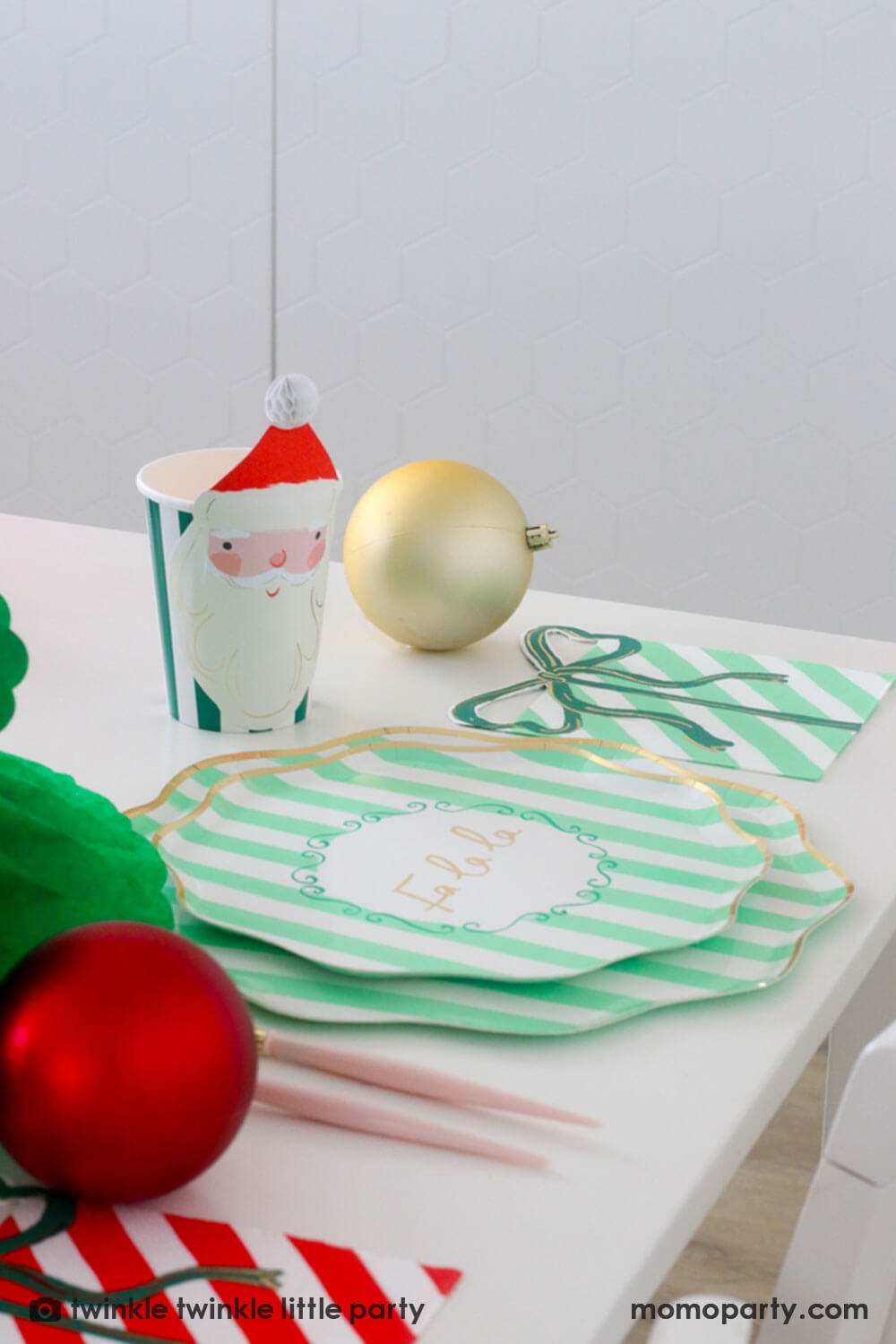 A festive Christmas party table featuring Momopartys's Festive mint striped dinner plates, side plates, present with a bow shaped napkins and Christmas honeycomb party cups in Santa design by Meri Meri. With gold and red Christmas ornament balls scattered around the table, making this a modern inspo for a festive Holiday table setting.