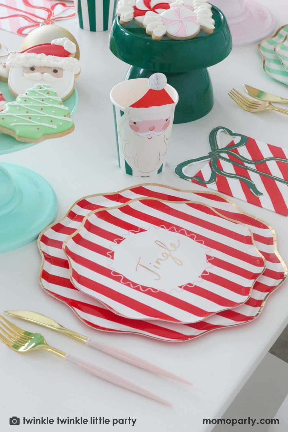 A festive Christmas party table featuring Momopartys's Festive striped dinner plates, side plates, present with a bow shaped napkins and Christmas honeycomb party cups in Santa design by Meri Meri. In the center of the table are a mint and green cake stand with festive Holiday cookies in the design of Peppermint, Santa, Christmas tree, candy cane and snowflake. Makes this a modern inspo for a festive Holiday table setting.