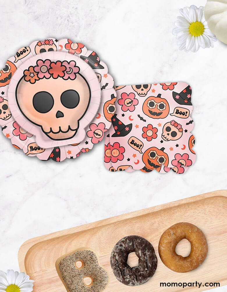A fall Halloween party table featuring Momopartys's 8" Groovy Halloween Icon Plates, 7" floral skull plates and 6.5" Groovy Halloween Napkins by Ellie's Party. Next to it are some donuts shaped as "BOO" for some Halloween spooky fun. This collection is perfect for a cute and stylish Halloween table setting. Featuring groovy pumpkins, skulls, flowers, and witch hats, this party collection is great for a pink Halloween bash or kid's boho Halloween birthday party!