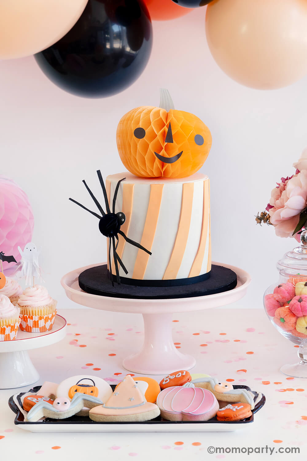 A halloween cake decorated with pumpkin honeycomb from Momopartys's Halloween Character Honeycomb set by Meri Meri. On the side of the cake, there's the small honeycomb spider. Along with pastel colored Halloween sugar cookies in the front, it makes it great Halloween treat ideas for a kid's friendly, not-so-scary Halloween party.