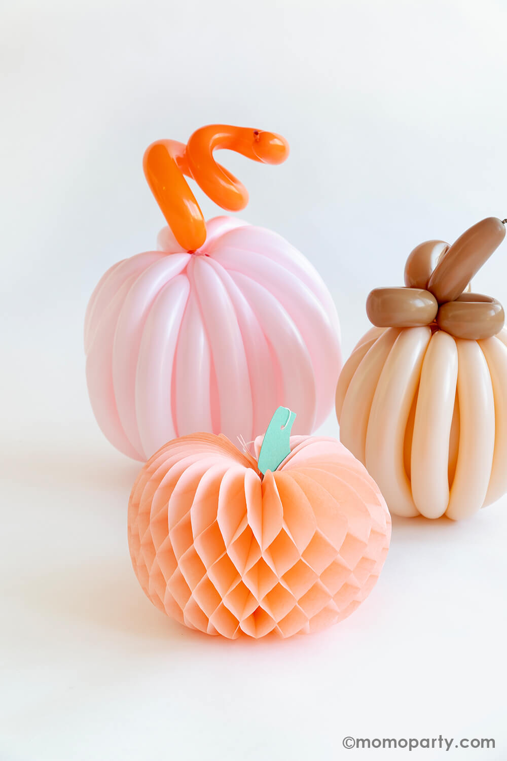 Two boho themed colored pumpkins made with twisting balloons, next to them is Momopartys's peach honeycomb decoration. All together they make a perfect fall decoration for an autumn gathering or Halloween bash.