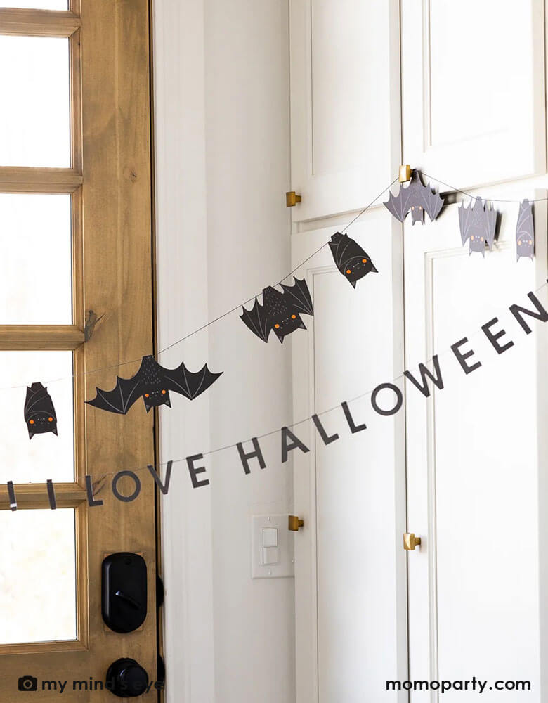 A door entrance decorated with Momopartys's 6' Freakin' Bats Garland by My Mind's Eye. This banner set includes a spooky stitched bat banner and a stitched word banner featuring the phrase "It's freakin bats! I love Halloween." These banners create a frightfully fun scene and sure to drive your guests batty this Halloween.